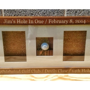 May include: A wooden frame with three compartments for displaying a golf ball and scorecard. The frame is engraved with "Jim's Hole In One / February 8, 2014" and "Whirlwind Golf Club / Devils Claw 14th Hole".
