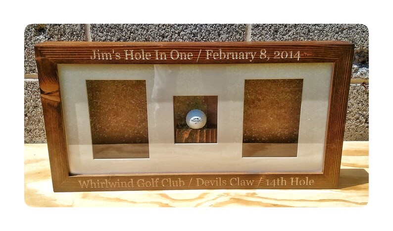 May include: A wooden frame with three compartments for displaying a golf ball and scorecard. The frame is engraved with "Jim's Hole In One / February 8, 2014" and "Whirlwind Golf Club / Devils Claw 14th Hole".