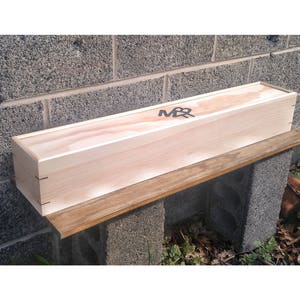 May include: A wooden box with the letters "M&R" engraved on the top. The box is sitting on a wooden shelf.