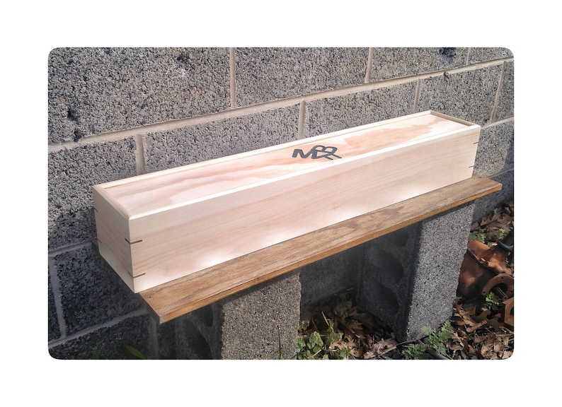 May include: A wooden box with the letters "M&R" engraved on the top. The box is sitting on a wooden shelf.