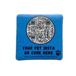 May include: A square, light blue block with a circular QR code in the center. The text "YOUR PET INSTA QR CODE HERE" is printed below the QR code, along with a paw print and the words "SANDY PAWS GOURMET DOG TREATS".
