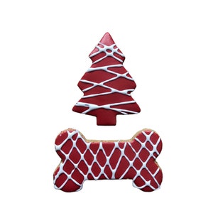 May include: Two dog treats: a red Christmas tree and a bone-shaped cookie. Both are decorated with white icing in a lattice pattern. The treats are on a white background.