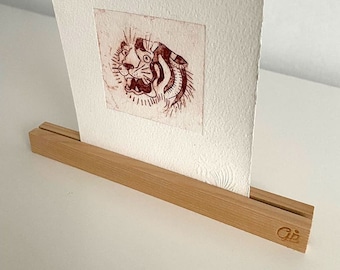 May include: A red and brown tiger print on white paper is displayed on a wooden easel with the text "Gjs" on the bottom right corner.
