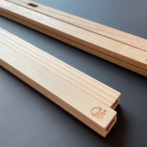 May include: Two wooden picture frames with a light wood finish. The frames are stacked on top of each other. The frames have a small hole on the top and bottom for hanging. The frames have a small logo on the side that says "Cij".