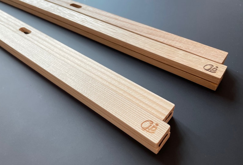 May include: Two wooden picture frames with a light wood finish. The frames are stacked on top of each other. The frames have a small hole on the top and bottom for hanging. The frames have a small logo on the side that says "Cij".