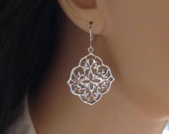 May include: Silver filigree dangle earrings with a square-shaped design. The earrings have a delicate, intricate pattern.