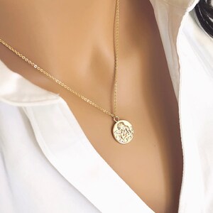 May include: A gold chain necklace with a round pendant featuring a detailed embossed design of two angels.