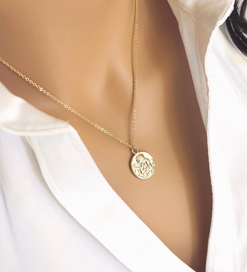 May include: A gold chain necklace with a round pendant featuring a detailed embossed design of two angels.