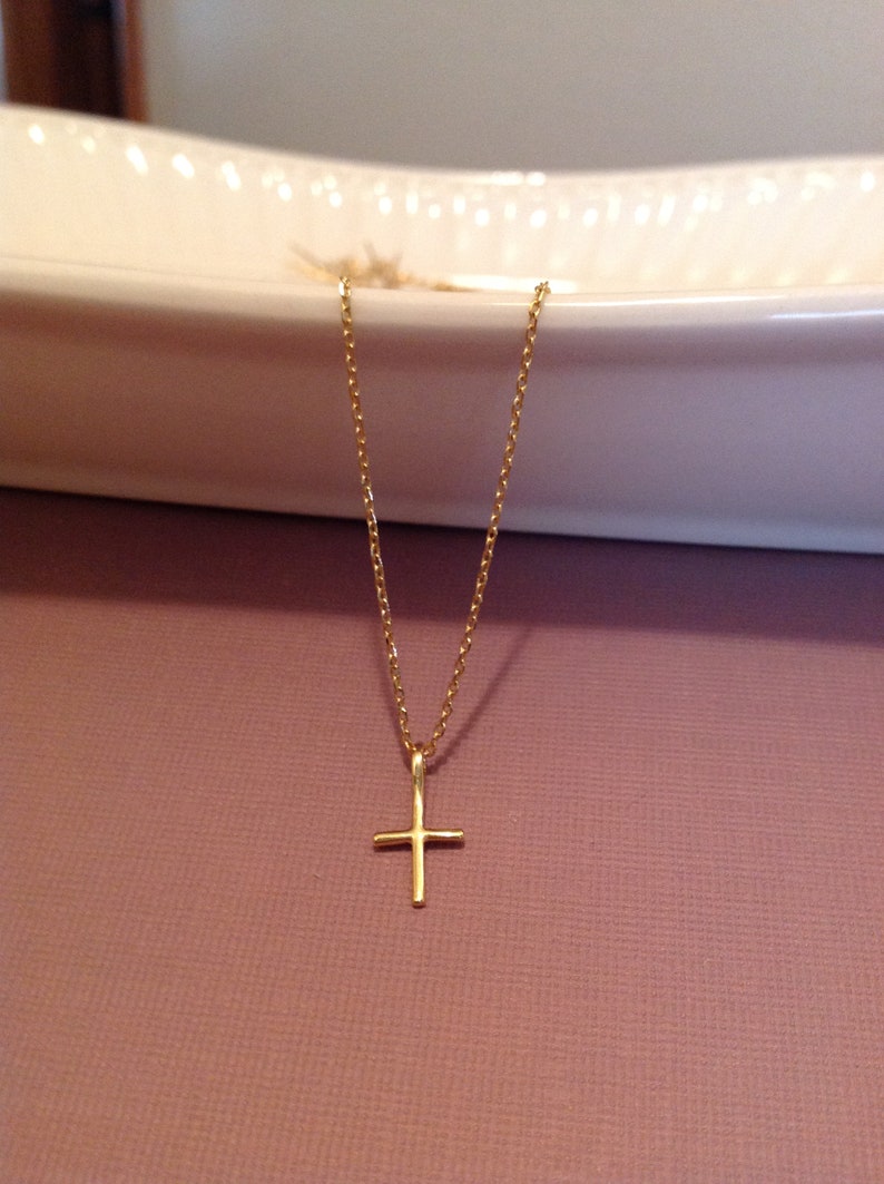 Pu&ograve; includere: Una collana a catena d'oro con un piccolo ciondolo a forma di croce d'oro.