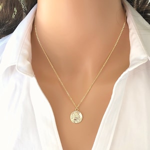 May include: A gold chain necklace with a round, textured pendant. The pendant features a detailed design.