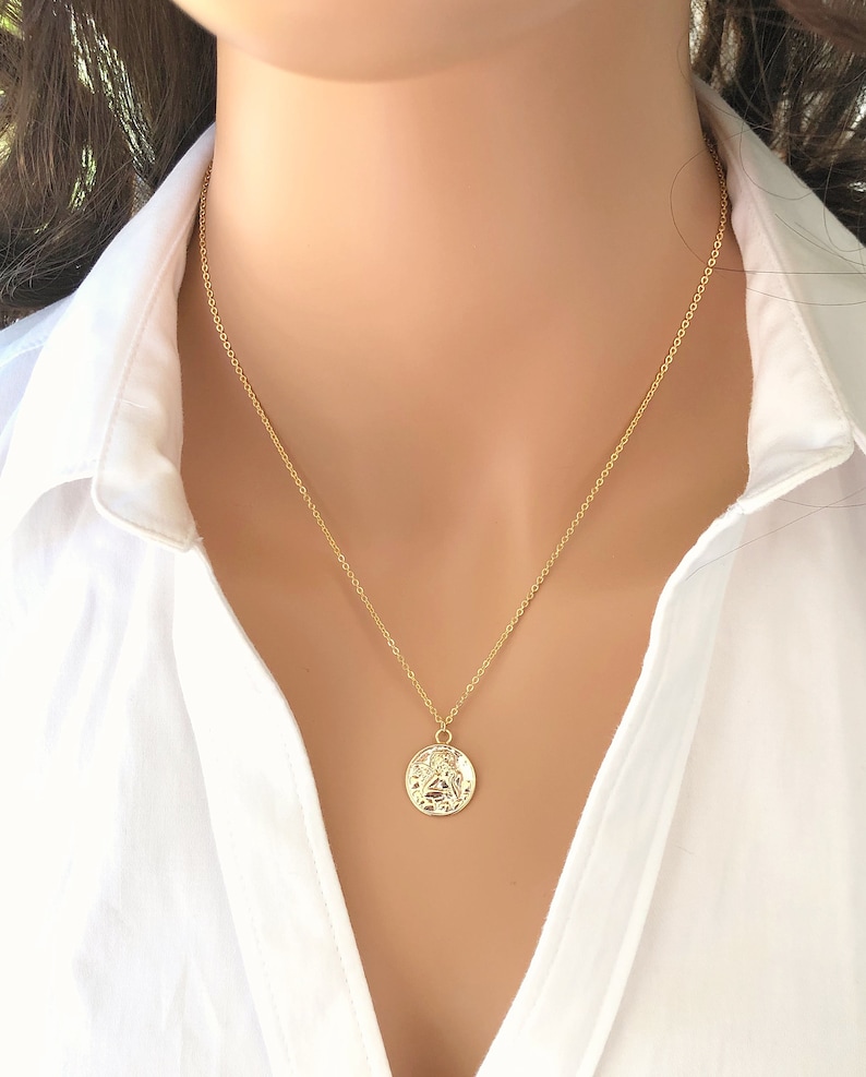 May include: A gold chain necklace with a round, textured pendant. The pendant features a detailed design.