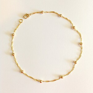 May include: A delicate gold chain anklet with small round beads. The chain is a twisted design and the anklet has a lobster claw clasp.