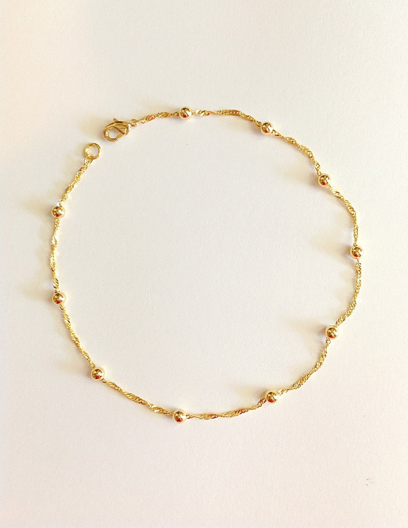 May include: A delicate gold chain anklet with small round beads. The chain is a twisted design and the anklet has a lobster claw clasp.