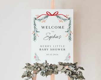 May include: Welcome to Sophia's Merry Little Baby Shower sign with a red ribbon and green foliage. The date of the shower is 03.12.2024.