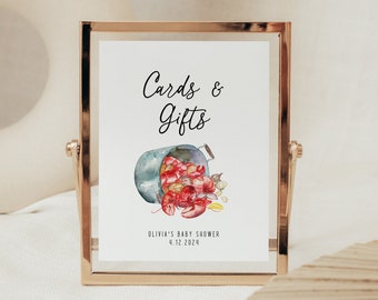 May include: A white sign with black text that reads "Cards & Gifts" and a watercolor illustration of a bucket of lobsters. The sign also includes the text "Olivia's Baby Shower 4.12.2024".