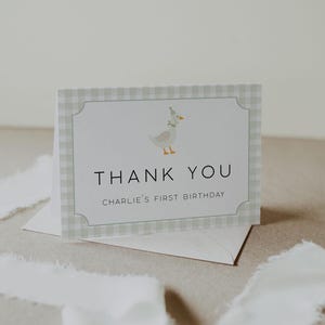 May include: A green and white gingham thank you card with a cartoon goose wearing a party hat. The text on the card reads "Thank You" and "Charlie's First Birthday".