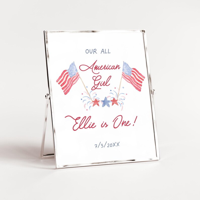 May include: A white framed sign with a red, white and blue American flag design. The text reads "Our All American Girl Ellie is One! 7/3/20XX".