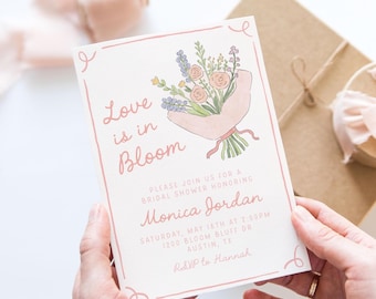 May include: A white rectangular bridal shower invitation with a pink border and a watercolor illustration of a flower bouquet. The text reads Love is in Bloom, Please join us for a bridal shower honoring Monica Jordan, Saturday, May 18th at 2:00pm, 1200 Bloom Bluff Dr, Austin, TX, RSVP to Hannah.