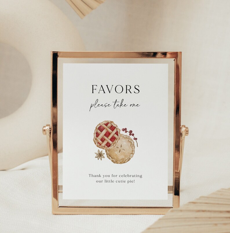 May include: A gold-framed sign with the text "Favors please take one" and a watercolor illustration of two pies. The text below the pies reads "Thank you for celebrating our little cutie pie!"
