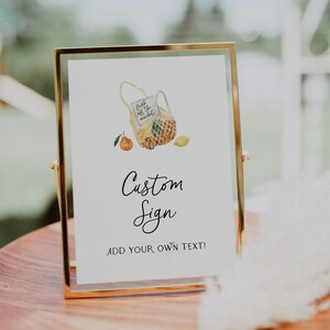 May include: A gold-framed sign with a watercolor illustration of a mesh bag filled with lemons and oranges. The text on the sign reads "fresh off the market" and "Custom Sign Add Your Own Text!"