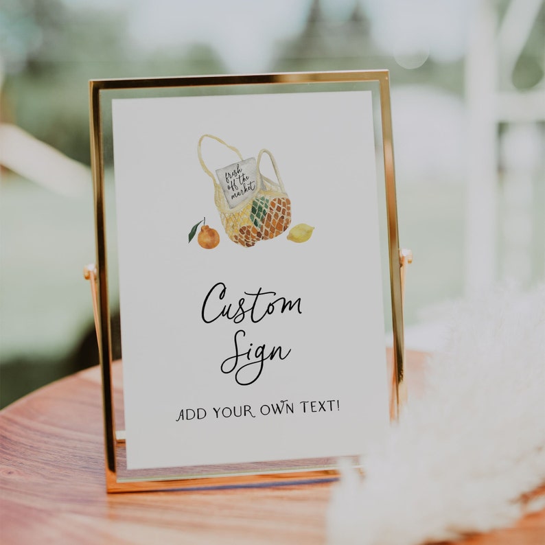 May include: A gold-framed sign with a watercolor illustration of a mesh bag filled with lemons and oranges. The text on the sign reads "fresh off the market" and "Custom Sign Add Your Own Text!"