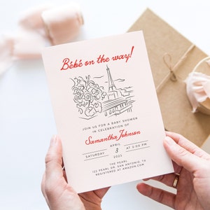 Op de afbeelding: Een roze babyborrel uitnodiging met een zwart-witte illustratie van de Eiffeltoren en bloemen. De tekst "B&eacute;b&eacute; on the way!" is rood. De uitnodiging bevat de datum, tijd en locatie van de borrel, evenals de naam van de aanstaande moeder, Samantha Johnson.