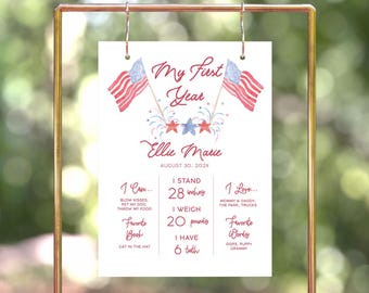 May include: A white sign with red, white, and blue watercolor American flags and fireworks. The sign reads "My First Year Ellie Marie August 30, 202X". The sign also lists the child's milestones, including height, weight, favorite book, and favorite words.