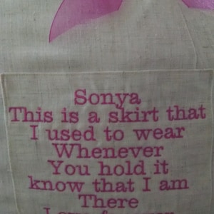 May include: A white fabric pillow with a pink ribbon and a pink embroidered message that reads: "Sonya This is a skirt that I used to wear Whenever You hold it know that I am There Love forever Mom"
