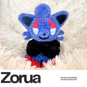 May include: A handmade blue crochet Zorua plushie with black accents, red details, and light blue eyes. The plushie has a black collar and red feet. The word "Zorua" is printed in bold black letters at the bottom of the image.