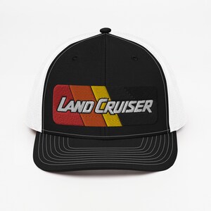 Puede incluir: Gorra de camionero negra y blanca con un parche bordado en rojo, naranja, amarillo y negro que dice "LAND CRUISER" en blanco.