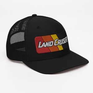 Puede incluir: Gorra de camionero negra con un parche a rayas rojo, naranja y amarillo que dice "LAND CRUISER" en blanco.
