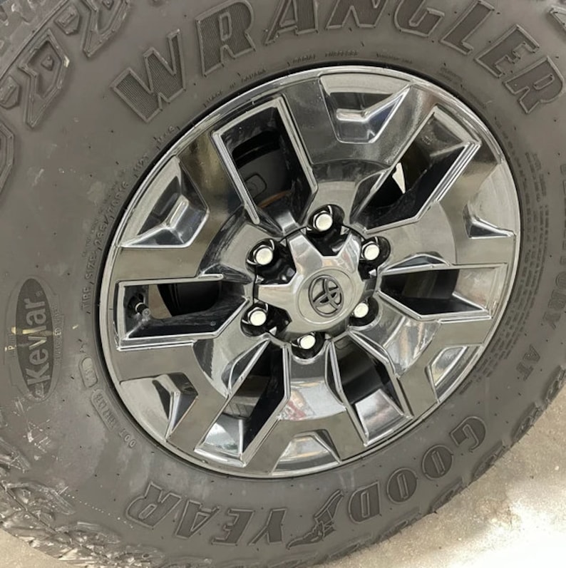 May include: Close-up of a black Toyota wheel with a silver Toyota emblem in the center. The tire is a Goodyear Wrangler with the word "Kevlar" visible on the sidewall.