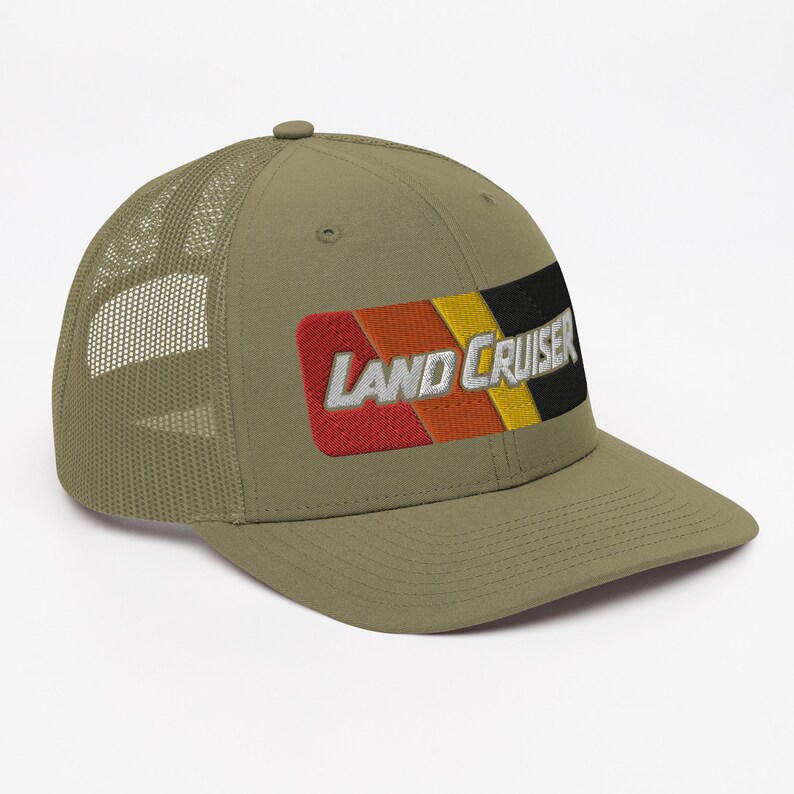 Puede incluir: Una gorra de camionero verde con un parche bordado en negro, amarillo, naranja y rojo que dice "LAND CRUISER".