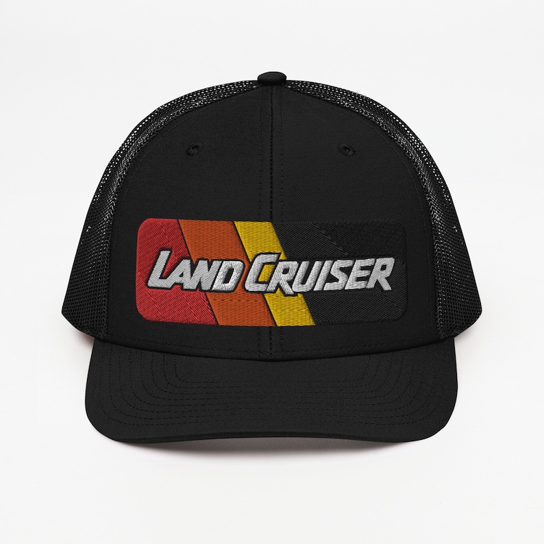 Puede incluir: Gorra de camionero negra con un parche a rayas rojo, naranja y amarillo que dice "LAND CRUISER" en letras blancas.