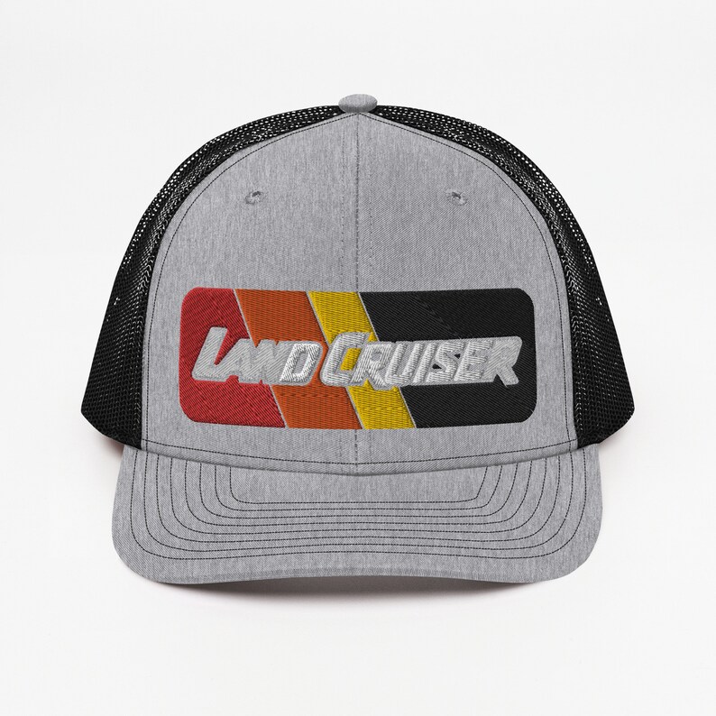 Puede incluir: Una gorra de camionero gris y negra con un parche bordado en rojo, naranja, amarillo y negro que dice "LAND CRUISER" en blanco.