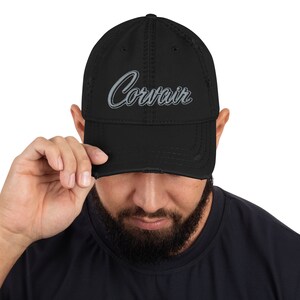 Könnte beinhalten: Eine schwarze, abgenutzte Baseballkappe mit einem grauen, gestickten "Corvair"-Logo.