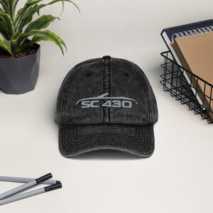 Könnte beinhalten: Eine schwarze Baseballkappe im Vintage-Stil mit einem weißen gestickten Design einer Autosilhouette und dem Text "SC 430".