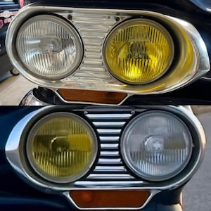 May include: Close-up of a vintage car's headlights. The headlights are round and have a chrome trim. The headlights are on and the light is shining through the glass. The car is blue and has a black grill.