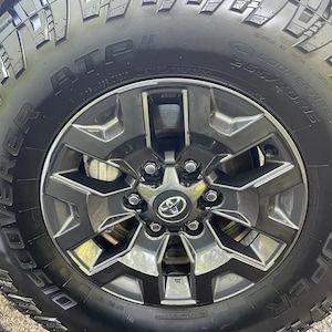 May include: Close-up of a black tire and a dark gray alloy wheel. The tire has the text "ATP" and "COOPER TIRES 265/70R15". The wheel has a Toyota logo in the center.