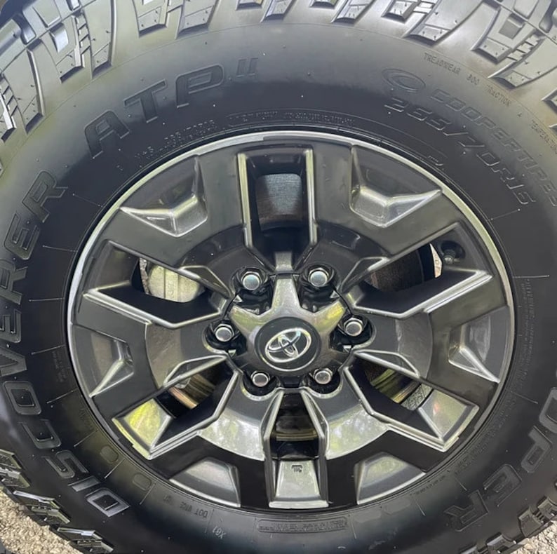 May include: Close-up of a black tire and a dark gray alloy wheel. The tire has the text "ATP" and "COOPER TIRES 265/70R15". The wheel has a Toyota logo in the center.