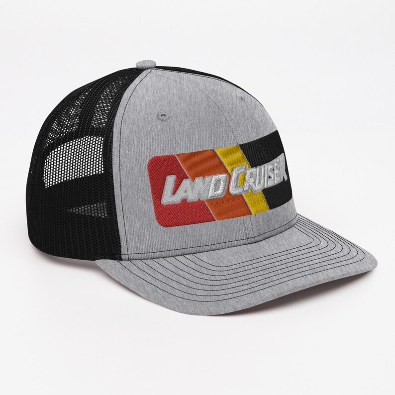 Puede incluir: Una gorra de camionero gris y negra con un parche bordado en rojo, naranja, amarillo y negro que dice "LAND CRUISER".