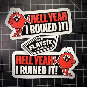 Peut inclure: Plusieurs autocollants avec des graphismes audacieux. Deux autocollants affichent le texte "HELL YEAH I RUINED IT!" avec un personnage de dessin animé rouge faisant un geste obscène. Un troisième autocollant affiche "FLATSIX GRAPHICS".