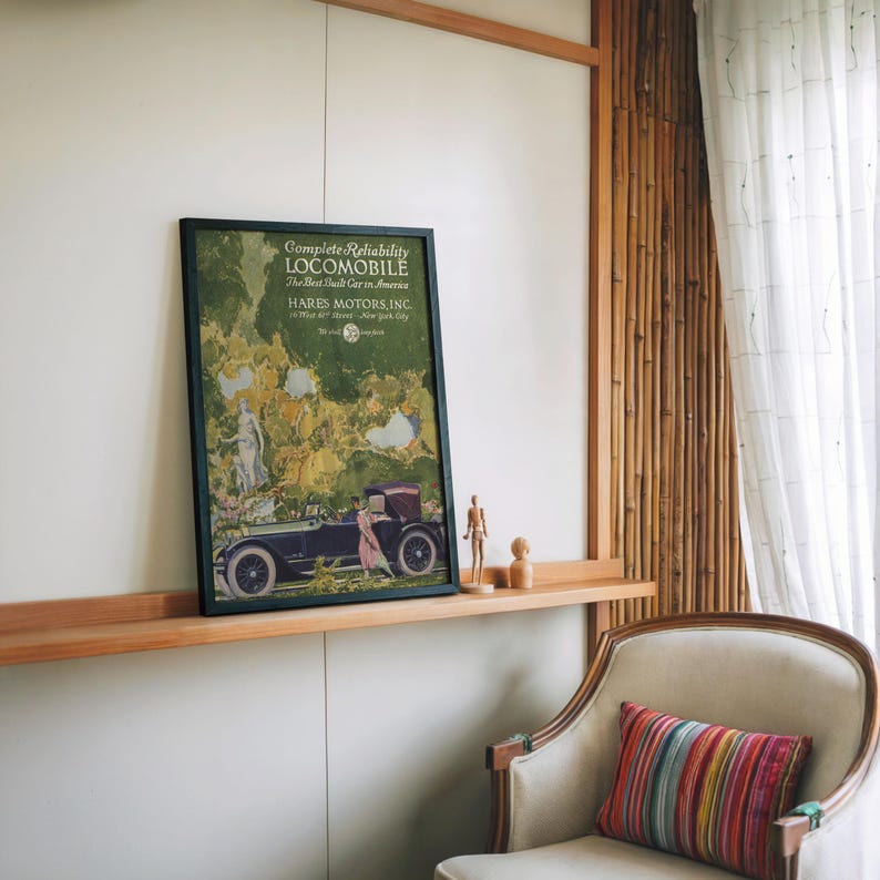 May include: A framed vintage advertisement for a Locomobile car, featuring a dark green frame and a colorful illustration of a car and figures. The text reads "Complete Reliability" and "HARES MOTORS, INC."