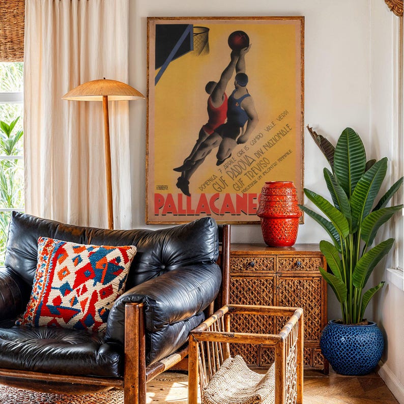 May include: An interior scene featuring a black leather armchair with a patterned pillow, a wooden side table, and a large framed vintage poster of a basketball game. A tall potted plant and a red ceramic vase add color.