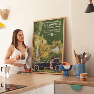May include: A framed vintage advertisement for a Locomobile car, featuring text and an illustration of a classic car. The ad is in a wooden frame and is displayed in a kitchen setting. The text reads "Complete Reliability LOCOMOBILE The Best Built Car in America".