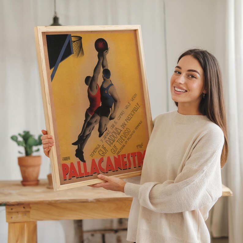 May include: A framed vintage basketball poster with a light wood frame. The poster features two players reaching for a basketball, with text in Italian. The poster has a yellow background with red, blue, and black accents.