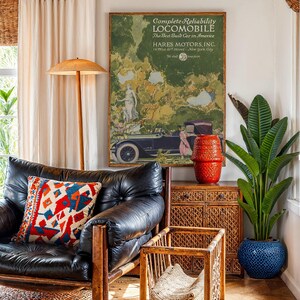 May include: An interior scene featuring a black leather armchair with a colorful patterned pillow. A vintage advertisement for a "LOCOMOBILE" car hangs on the wall. A red textured vase sits atop a woven cabinet, and a large potted plant adds greenery.