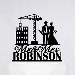 May include: Black silhouette of a bride and groom standing in front of a building under construction. The groom is wearing a hard hat and holding a blueprint. The bride is holding a bouquet of flowers. The text "Mr & Mrs ROBINSON" is below the couple.