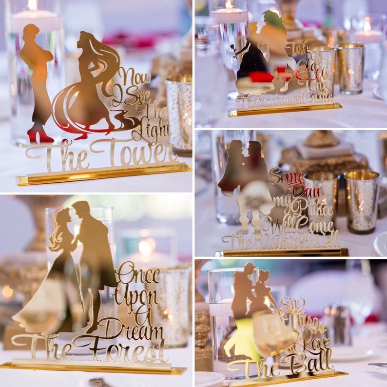 May include: Four gold mirror-like centerpieces featuring Disney princess silhouettes and quotes from the movies. The centerpieces are "Now I See the Light The Tower", "Some Day My Prince Will Come The Wishing Well", "Once Upon a Dream The Forest", and "Say Yes to This Love The Ball".