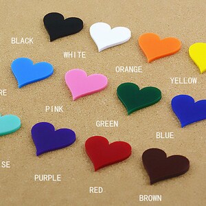 May include: A collection of 12 heart-shaped acrylic pieces in various colors, including black, white, orange, yellow, azure, pink, green, blue, turquoise, purple, red, and brown. Each heart is labeled with its corresponding color.